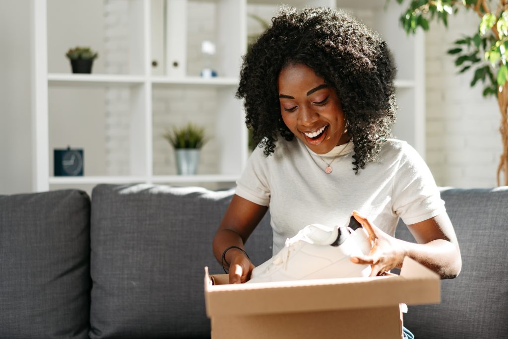 Young african woman sit on couch at home unpacking parcel cardboard box with online purchase, close up